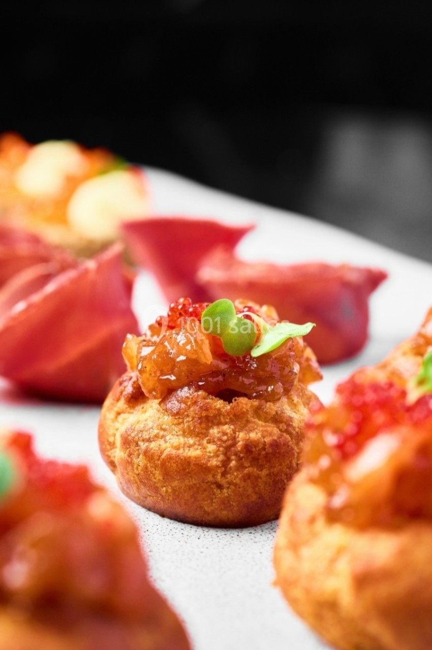Choux garnis de confit d'oignons, œufs de poisson et micro-pousses, présentés sur une assiette blanche.