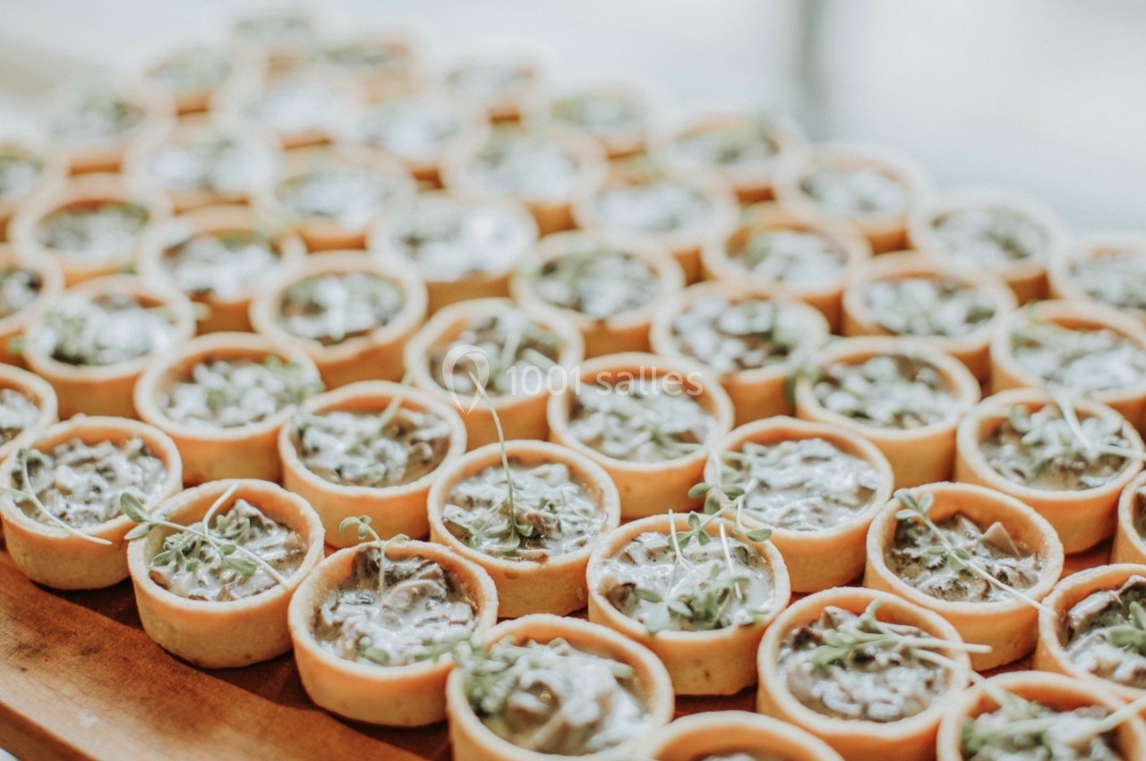Petites tartelettes garnies d'une préparation crémeuse et décorées de pousses vertes, disposées sur un plateau en bois.