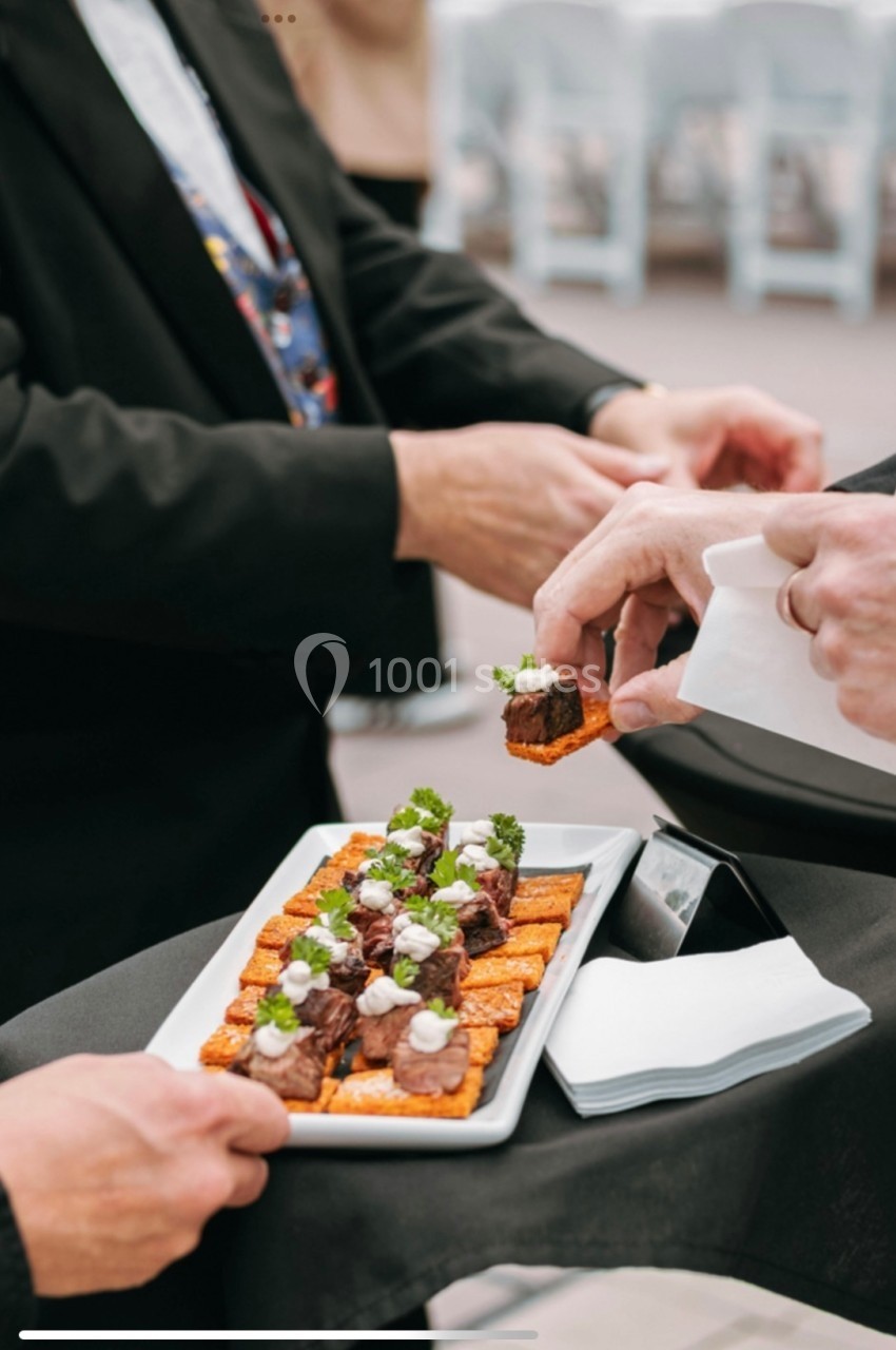 Un serveur présente un plateau de bouchées garnies de viande et d'herbes fraîches lors d'un événement.