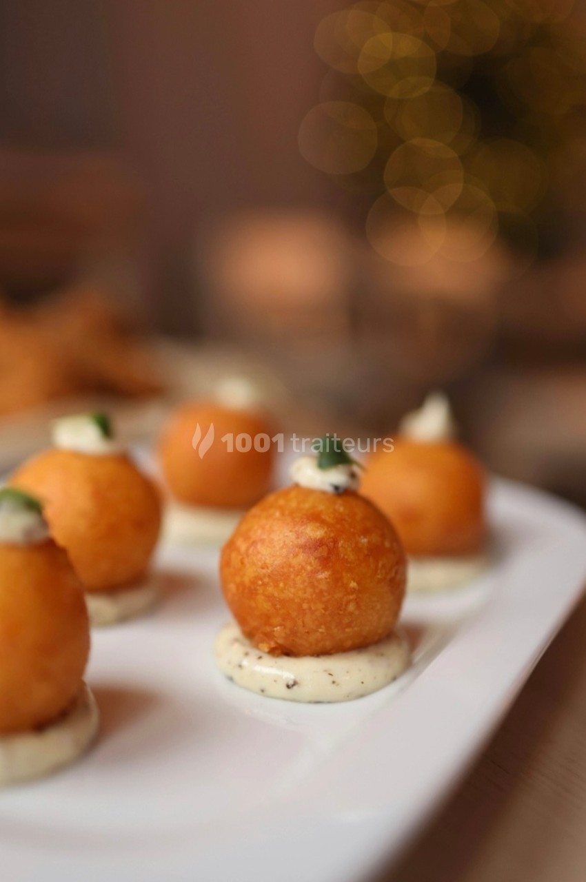 Bouchées apéritives dorées posées sur une sauce blanche, servies sur une assiette blanche dans un décor chaleureux.