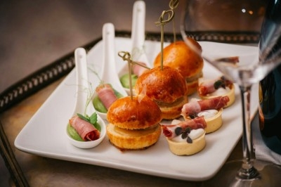 Bouchées apéritives élégantes surmontées de feuilles et de miettes croustillantes, disposées en rangées sur un plateau blanc.