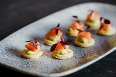 Bouchées apéritives élégantes surmontées de feuilles et de miettes croustillantes, disposées en rangées sur un plateau blanc.