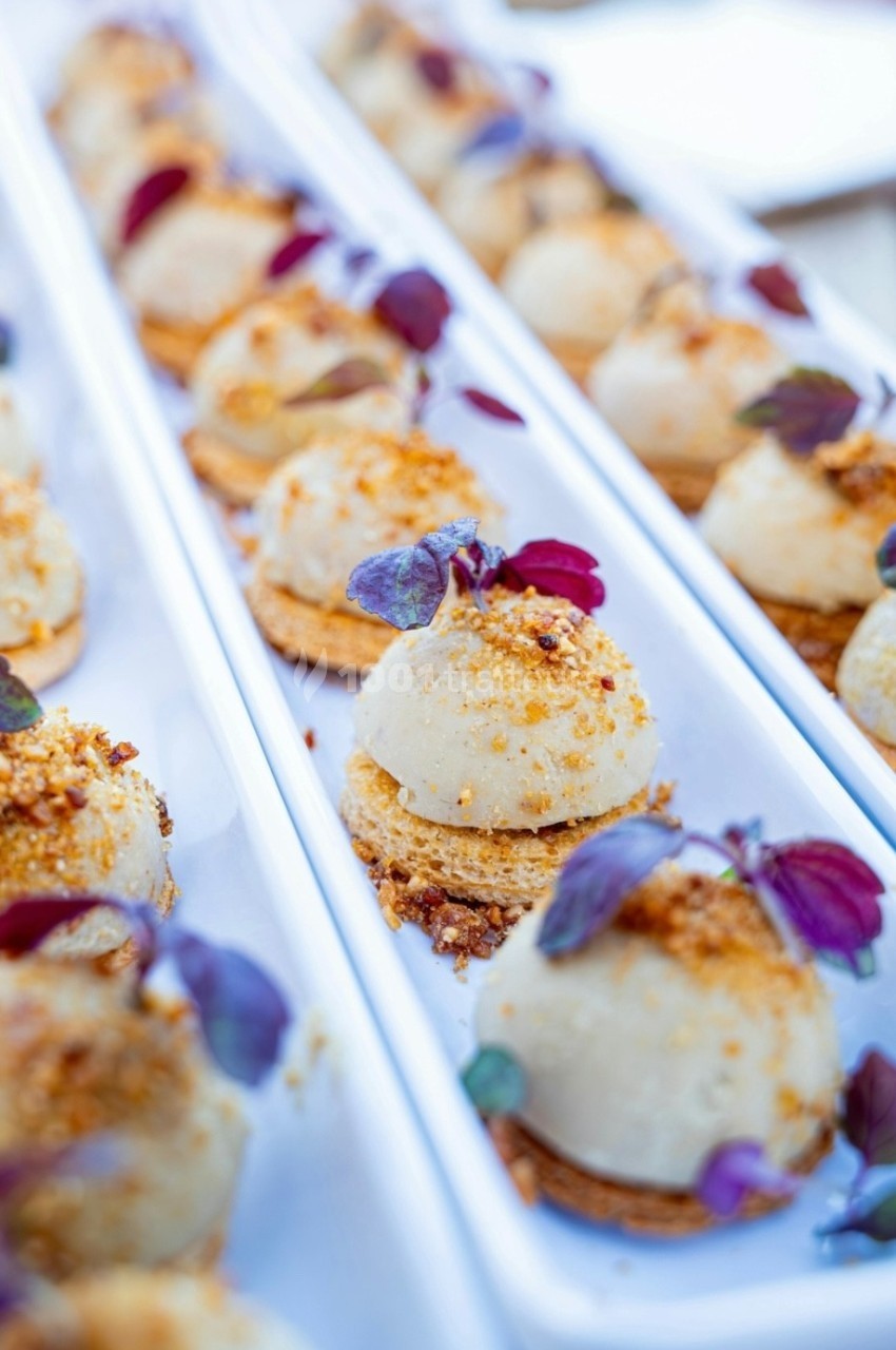 Bouchées apéritives élégantes surmontées de feuilles et de miettes croustillantes, disposées en rangées sur un plateau blanc.