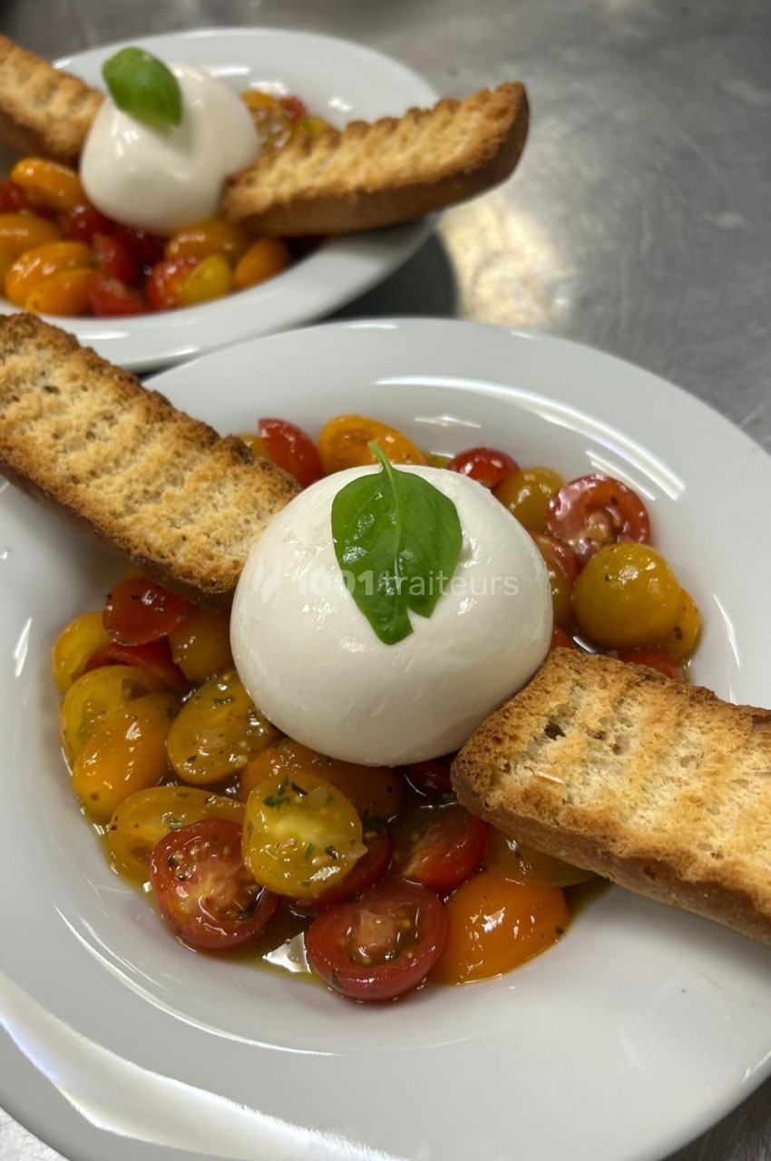 Assiette de tomates cerises colorées avec une boule de mozzarella, deux croûtons grillés et une feuille de basilic.