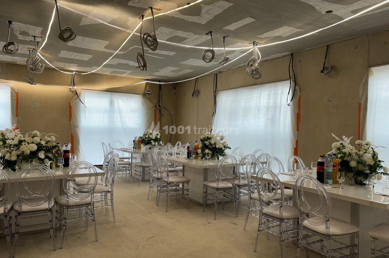 Salle en cours d'aménagement avec des tables décorées de fleurs blanches et des chaises transparentes.