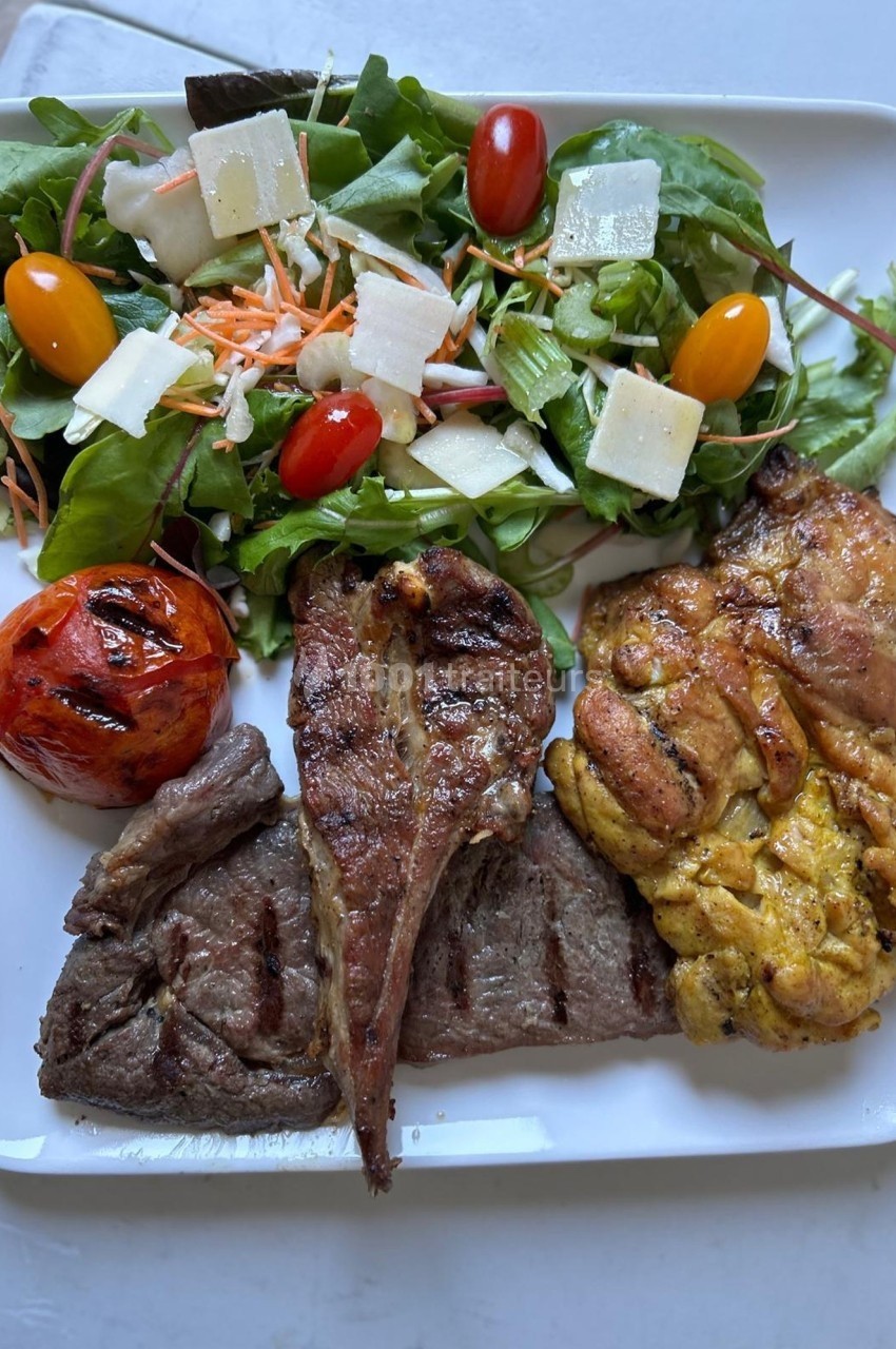 Assiette composée de viande grillée, salade verte avec tomates cerises, fromage, carottes râpées et tomate grillée.