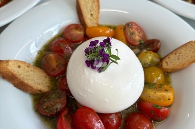 Miniature Traiteur Crosne (Essonne) - Aux Tulipes Traiteur #8 Assiette de burrata garnie de tomates cerises colorées et décorée d'une fleur violette sur une table blanche.
