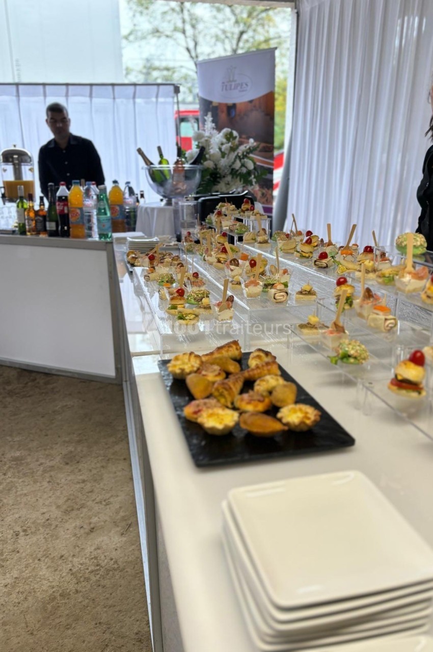 Buffet de cocktails avec une variété de bouchées et boissons disposées sur une table blanche dans un espace lumineux.
