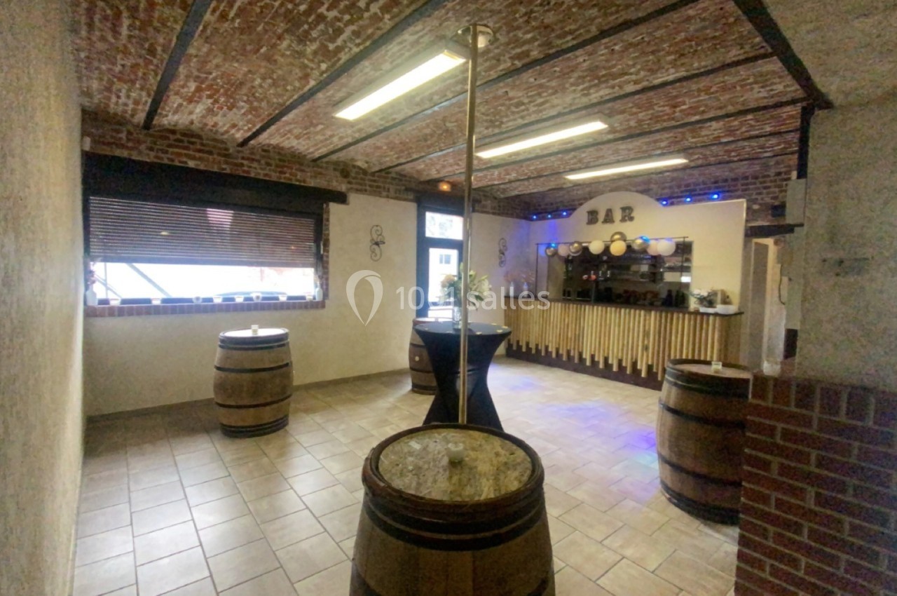Salle avec un bar en bois, des tonneaux utilisés comme tables et un plafond en briques apparentes.