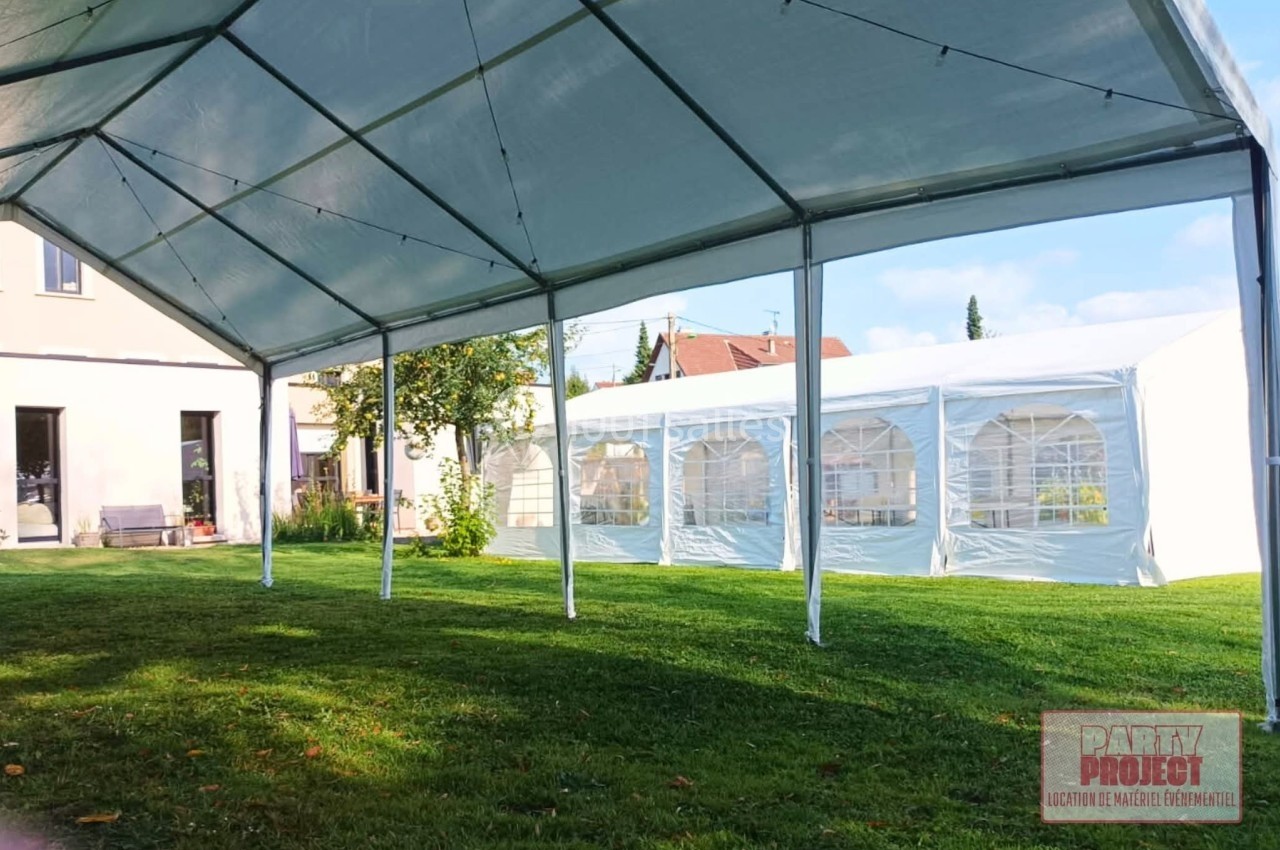 Structure de tentes blanches installées sur une pelouse, avec des bâtiments résidentiels en arrière-plan.