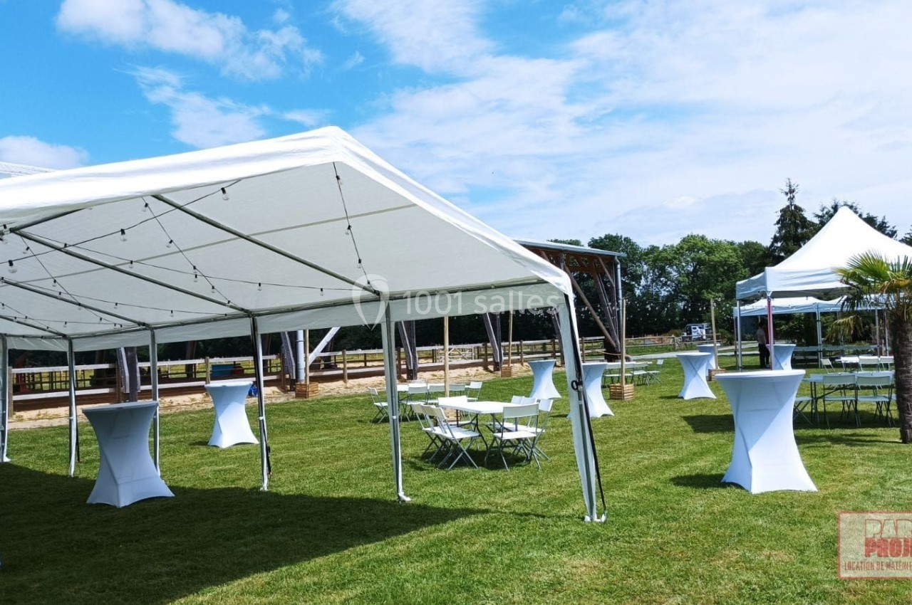 Tentes blanches montées sur une pelouse, entourées de tables et mange-debout, sous un ciel dégagé.