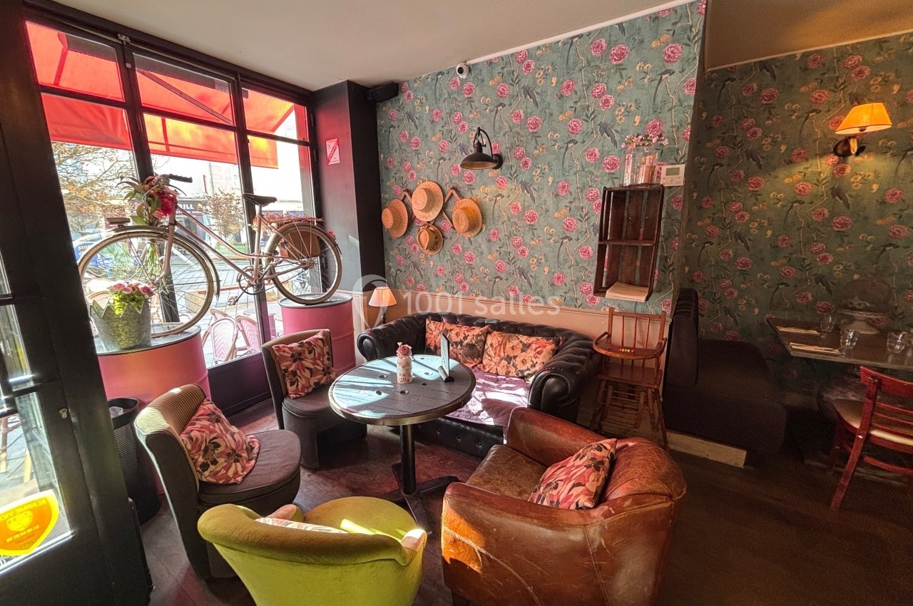 Salon de thé cosy avec fauteuils colorés, décoration florale, vélo suspendu et lumière naturelle.