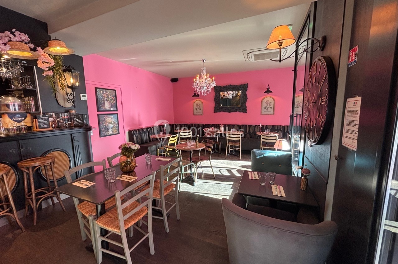 Salle de restaurant lumineuse avec murs roses, mobilier en bois et éléments décoratifs élégants.