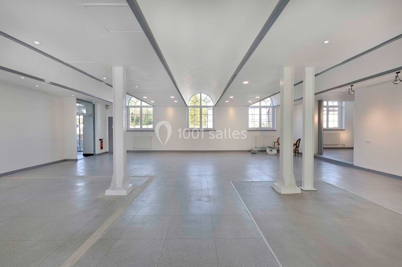 Intérieur d'un grand espace lumineux avec des colonnes blanches, un sol carrelé et de grandes fenêtres laissant entrer la…