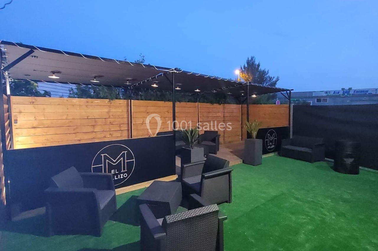 Terrasse extérieure avec chaises en rotin noir, pelouse artificielle et panneaux en bois sous un ciel au crépuscule.