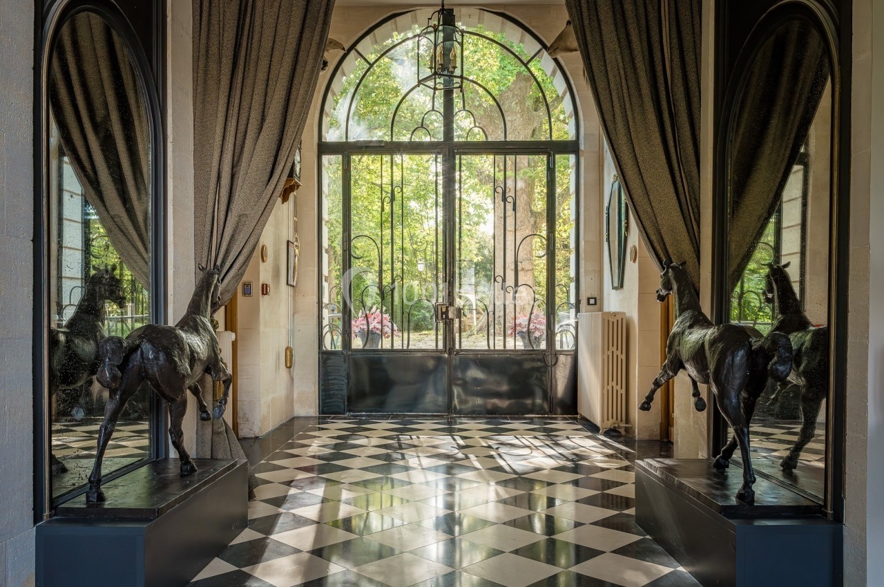 Entrée élégante avec sol en damier, statues de chevaux noirs et grande porte vitrée donnant sur un jardin verdoyant.