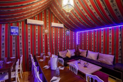 Salle décorée avec des tables rondes et chaises blanches, mur peint représentant une plage avec cabane et palmiers.