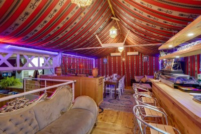 Salle décorée avec des tables rondes et chaises blanches, mur peint représentant une plage avec cabane et palmiers.