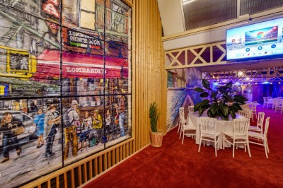 Salle décorée avec des tables rondes et chaises blanches, mur peint représentant une plage avec cabane et palmiers.