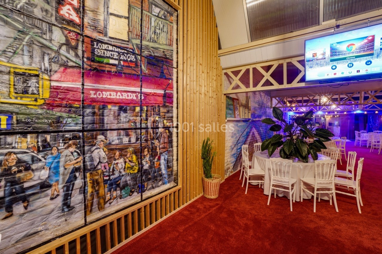 Salle décorée avec des peintures murales colorées, des tables blanches et un écran suspendu affichant une présentation.