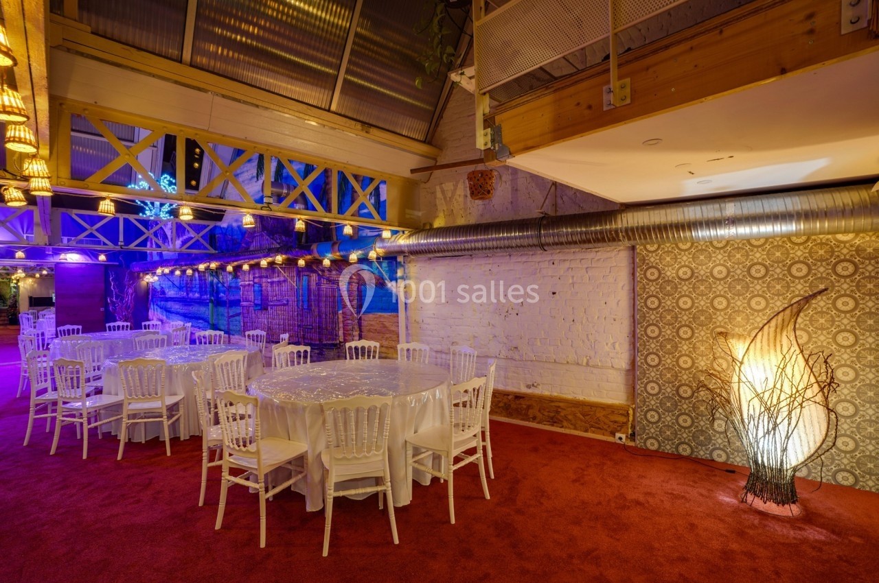 Salle décorée avec des tables rondes, chaises blanches, éclairage chaleureux et murs en briques apparentes.
