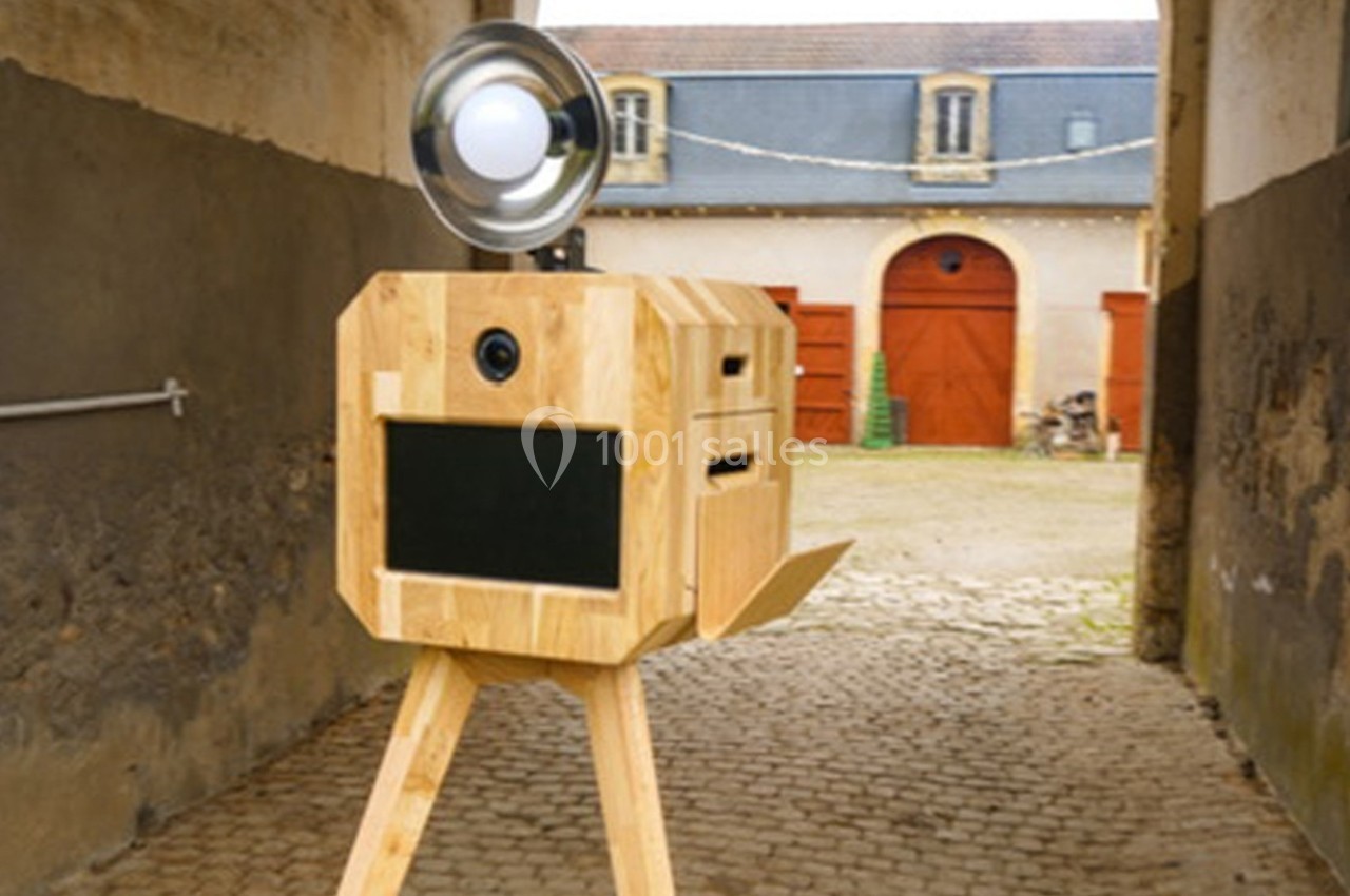 Appareil photo en bois sur trépied avec lampe circulaire, installé dans une cour pavée devant des bâtiments anciens.