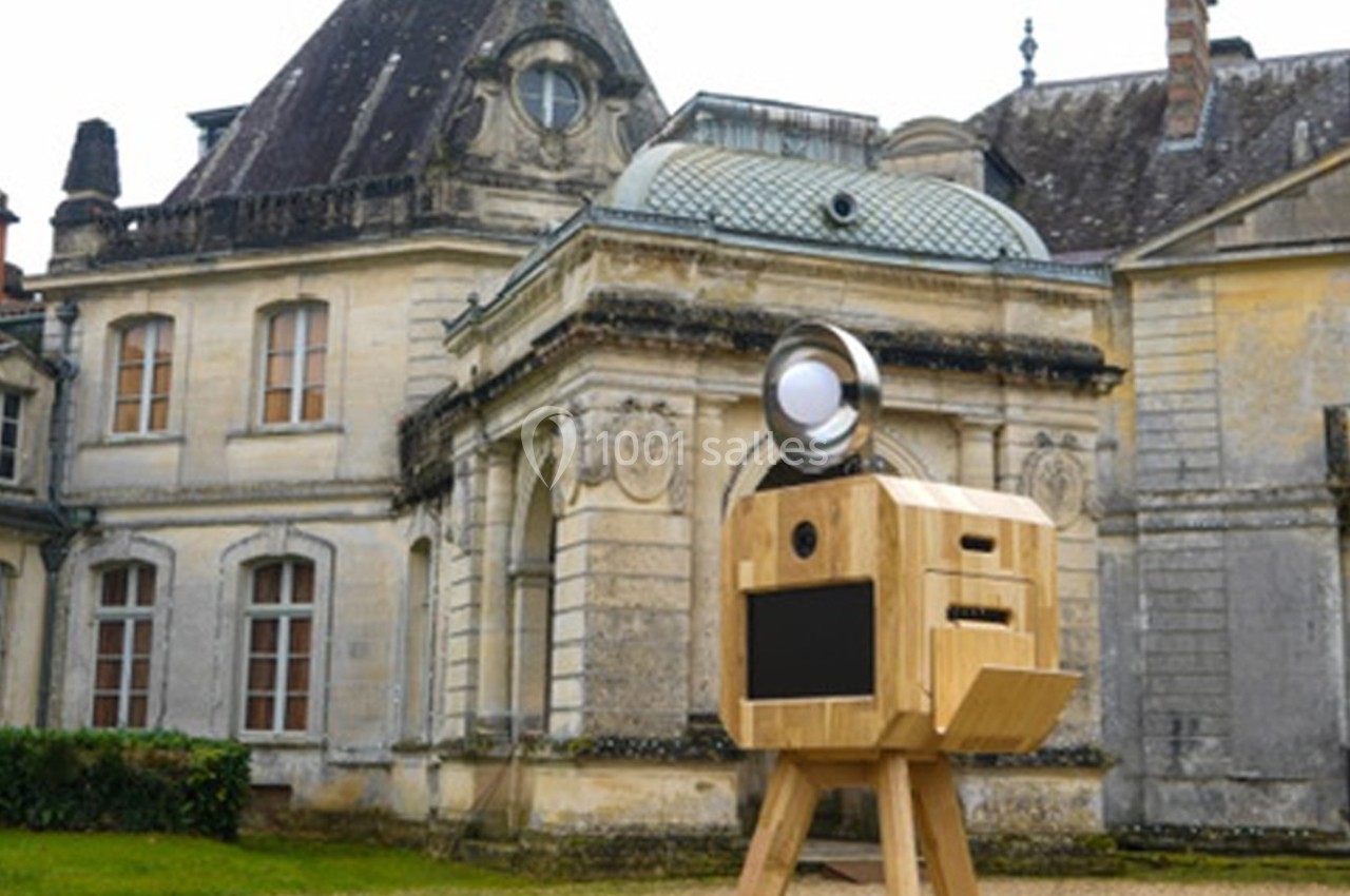 Cabine photo en bois sur trépied devant un bâtiment ancien en pierre avec des toits mansardés.