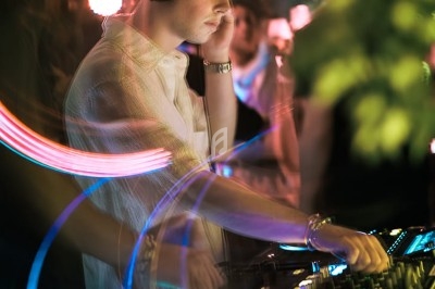 Un DJ mixe dans une ambiance de boîte de nuit avec des faisceaux lumineux et une foule floue en arrière-plan.