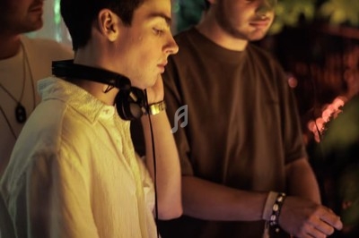 Un DJ mixe dans une ambiance de boîte de nuit avec des faisceaux lumineux et une foule floue en arrière-plan.