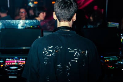 Un DJ mixe dans une ambiance de boîte de nuit avec des faisceaux lumineux et une foule floue en arrière-plan.