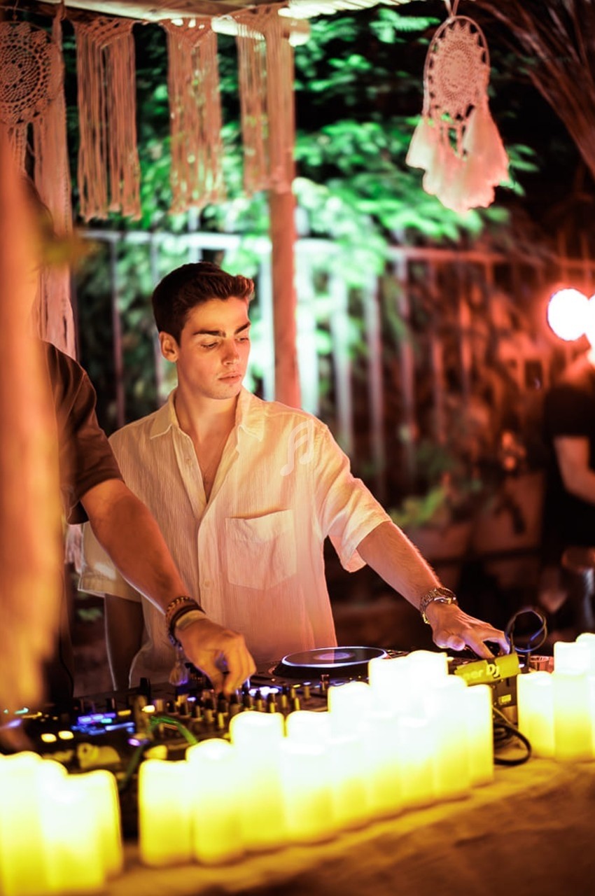 Un DJ mixe de la musique en extérieur, entouré de bougies LED et de décorations suspendues.