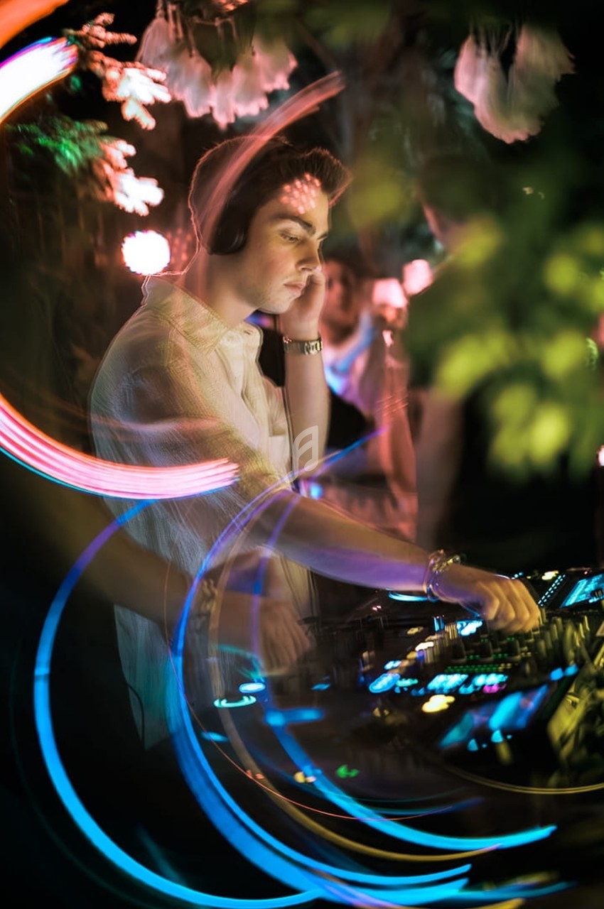 Un DJ mixe de la musique en soirée, entouré de lumières colorées et d'effets lumineux.