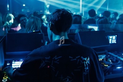 Miniature DJ Albigny-sur-Saône (Rhône) - Teebow #3 Un DJ mixe devant une foule dans une boîte de nuit éclairée par des lumières roses et des boules à facettes.