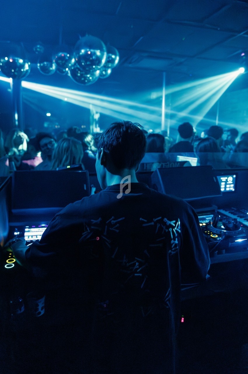 Un DJ mixe dans une boîte de nuit sombre, éclairée par des lumières bleues et des boules à facettes.