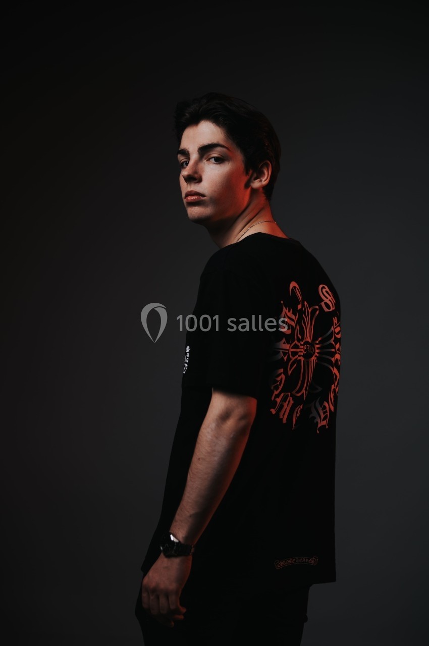Jeune homme de profil portant un t-shirt noir avec un motif graphique rouge dans un éclairage sombre.