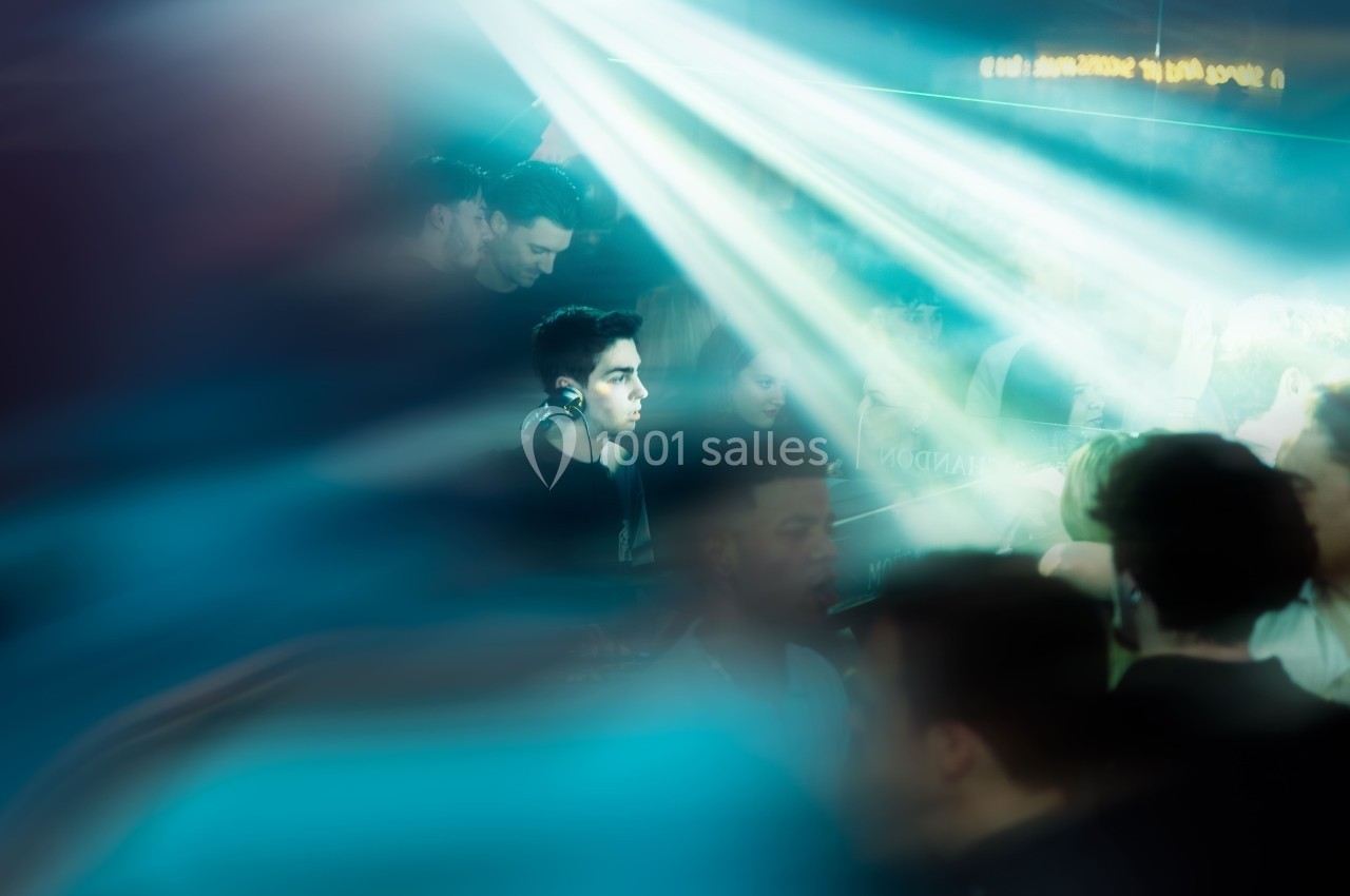 Un DJ mixe dans une ambiance de boîte de nuit avec des faisceaux lumineux et une foule floue en arrière-plan.