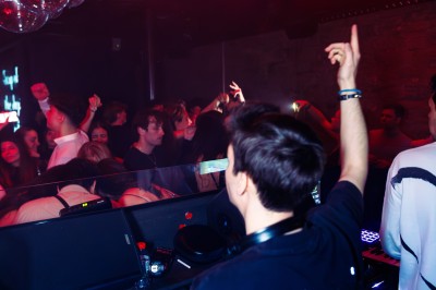 Miniature DJ Albigny-sur-Saône (Rhône) - Teebow #5 Un DJ mixe devant une foule dans une boîte de nuit éclairée par des lumières roses et des boules à facettes.