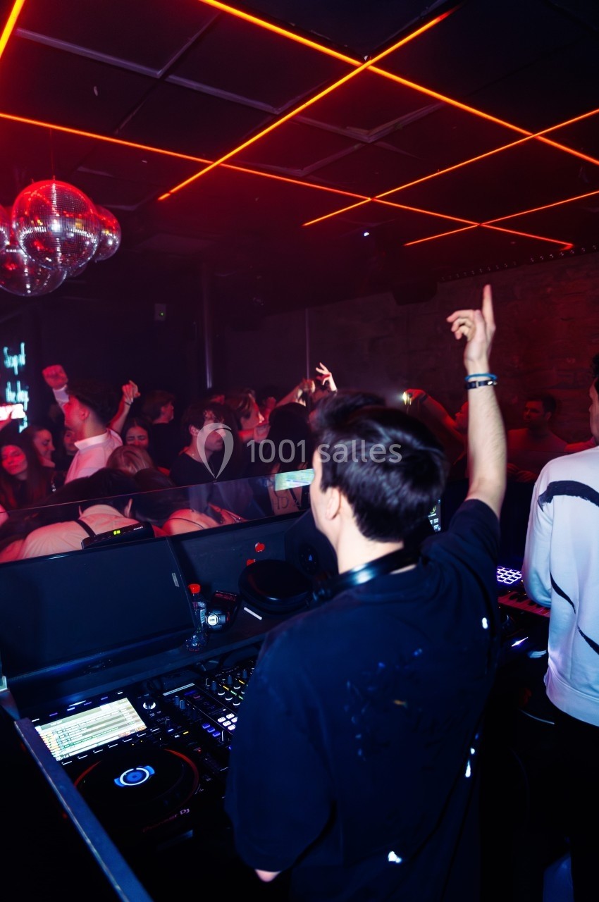 Un DJ mixe dans une boîte de nuit animée sous des lumières rouges et des boules à facettes.