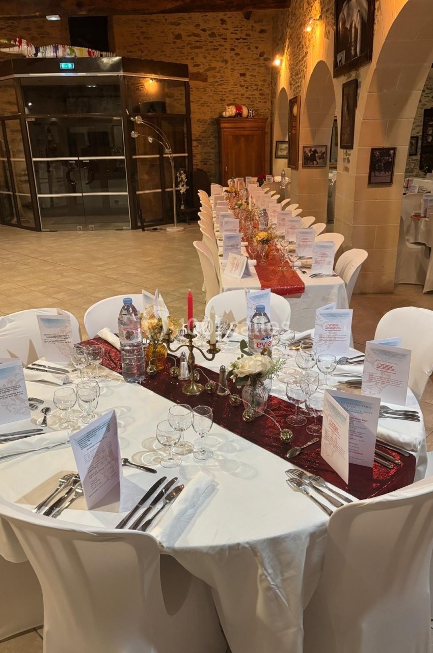 Salle de réception avec tables rondes dressées, nappes blanches, menus, chandeliers et décorations élégantes.