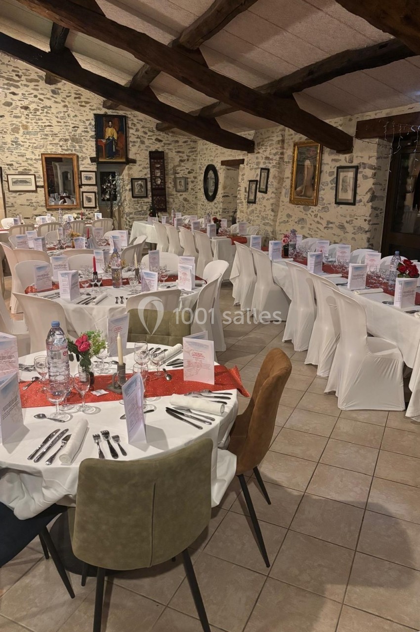 Salle de réception décorée avec des tables rondes dressées, nappes blanches, chemins de table rouges et menus disposés.