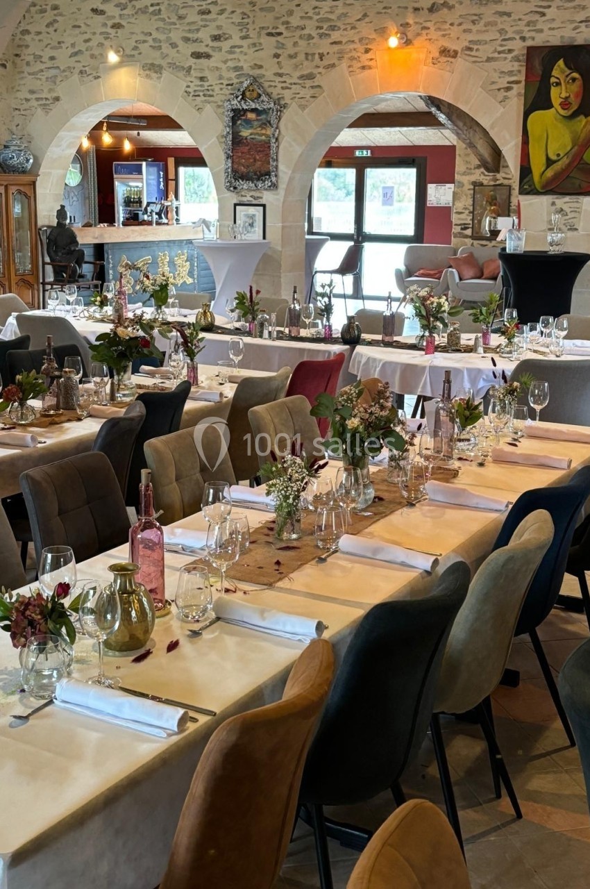 Salle de réception décorée avec des tables dressées, ornées de fleurs et de bougies, dans un cadre en pierre.