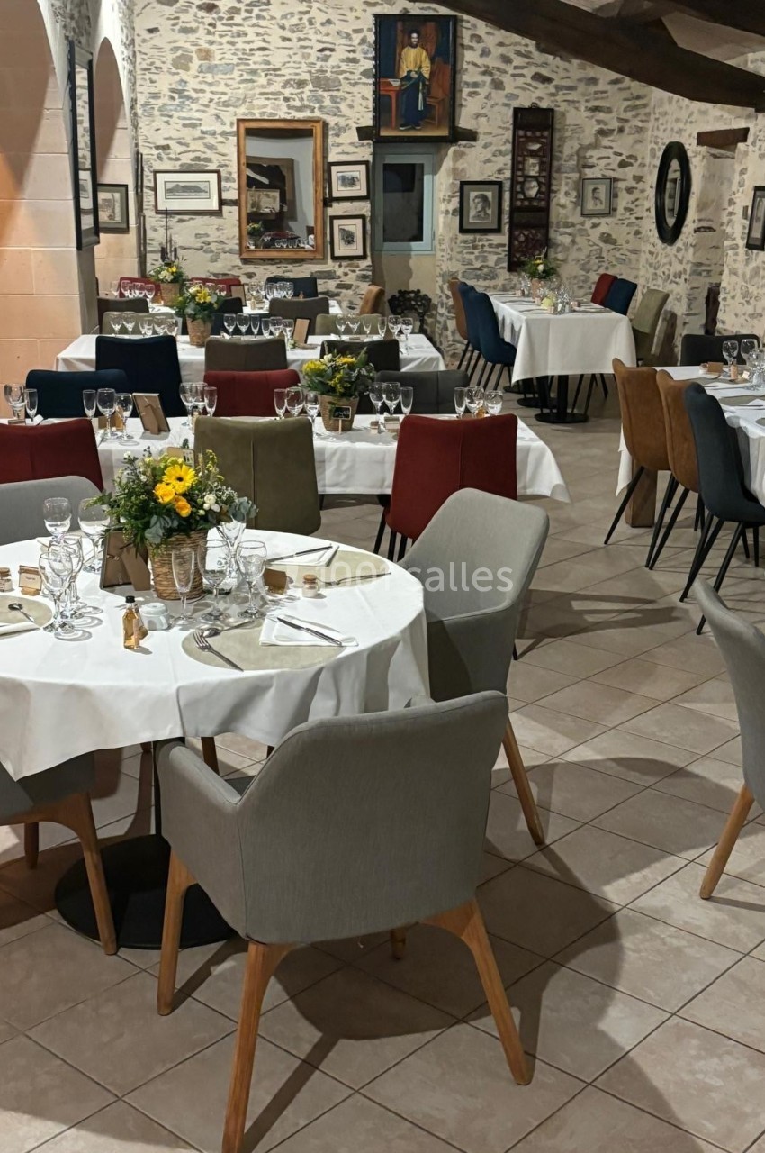 Salle de restaurant élégante avec tables dressées, nappes blanches, chaises colorées et décor mural en pierre.