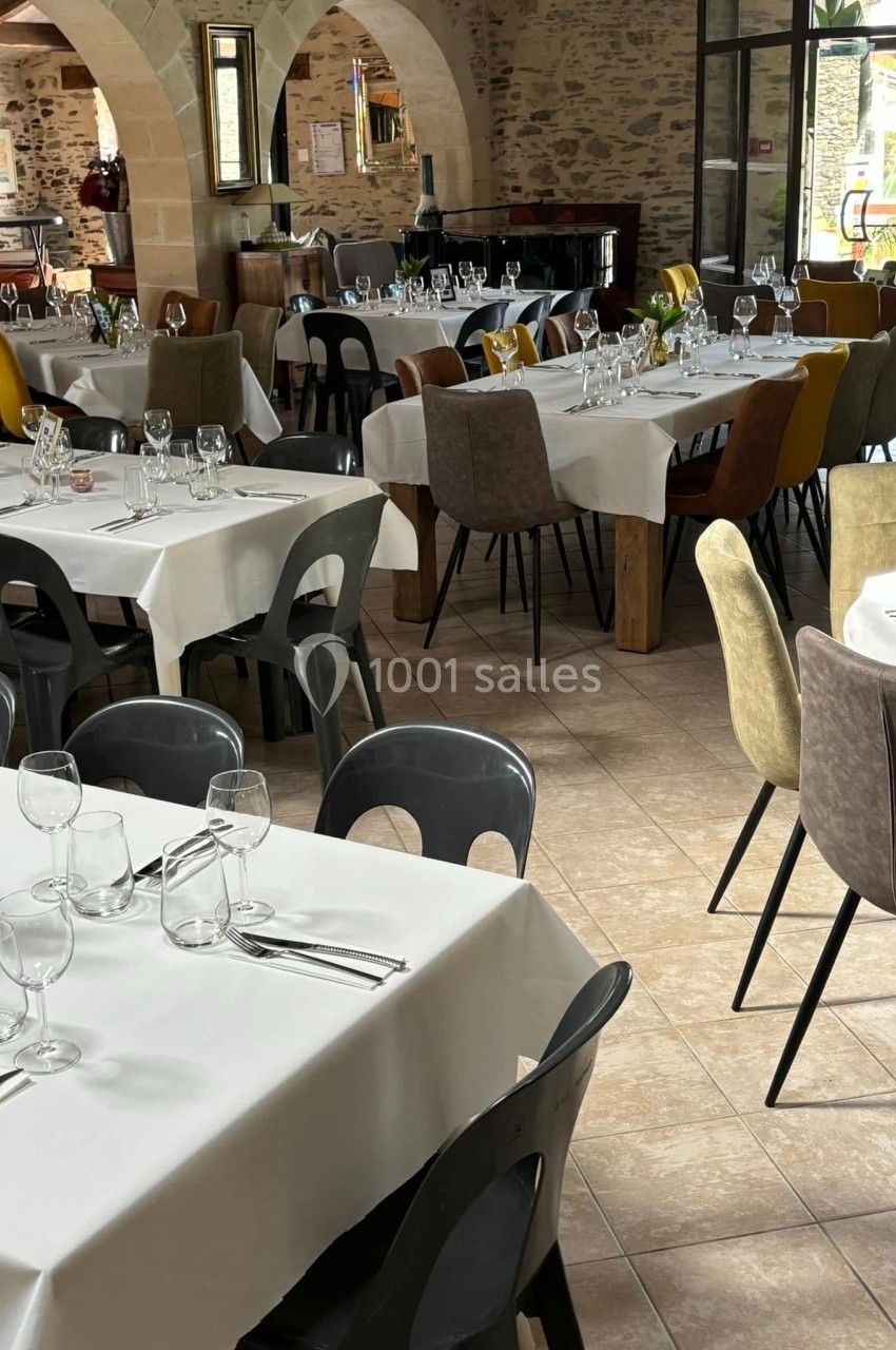 Salle de restaurant lumineuse avec tables dressées, nappes blanches, verres et couverts, entourées de chaises variées.