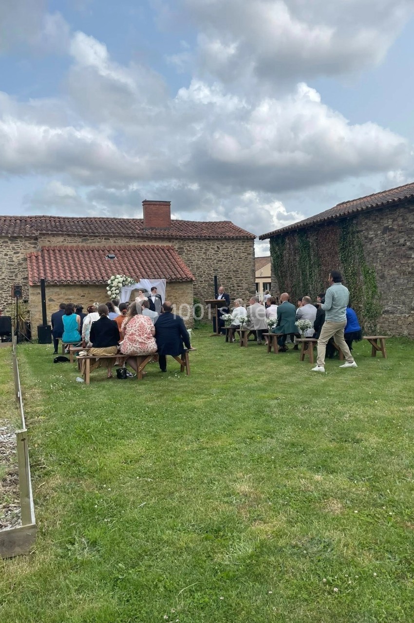 Cérémonie en plein air avec des invités assis sur des bancs, devant un autel décoré, dans une cour entourée de bâtiments en…