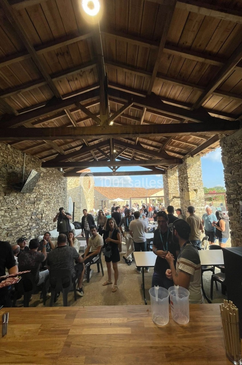 Des personnes discutent et partagent un repas sous une structure en bois et pierre, dans un espace ouvert et lumineux.