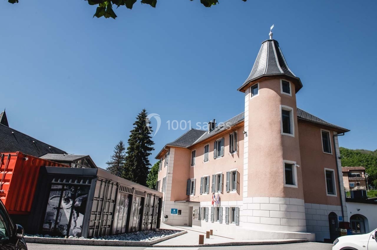 Bâtiment historique avec une tour, entouré de conteneurs modernes et d'arbres, sous un ciel bleu dégagé.