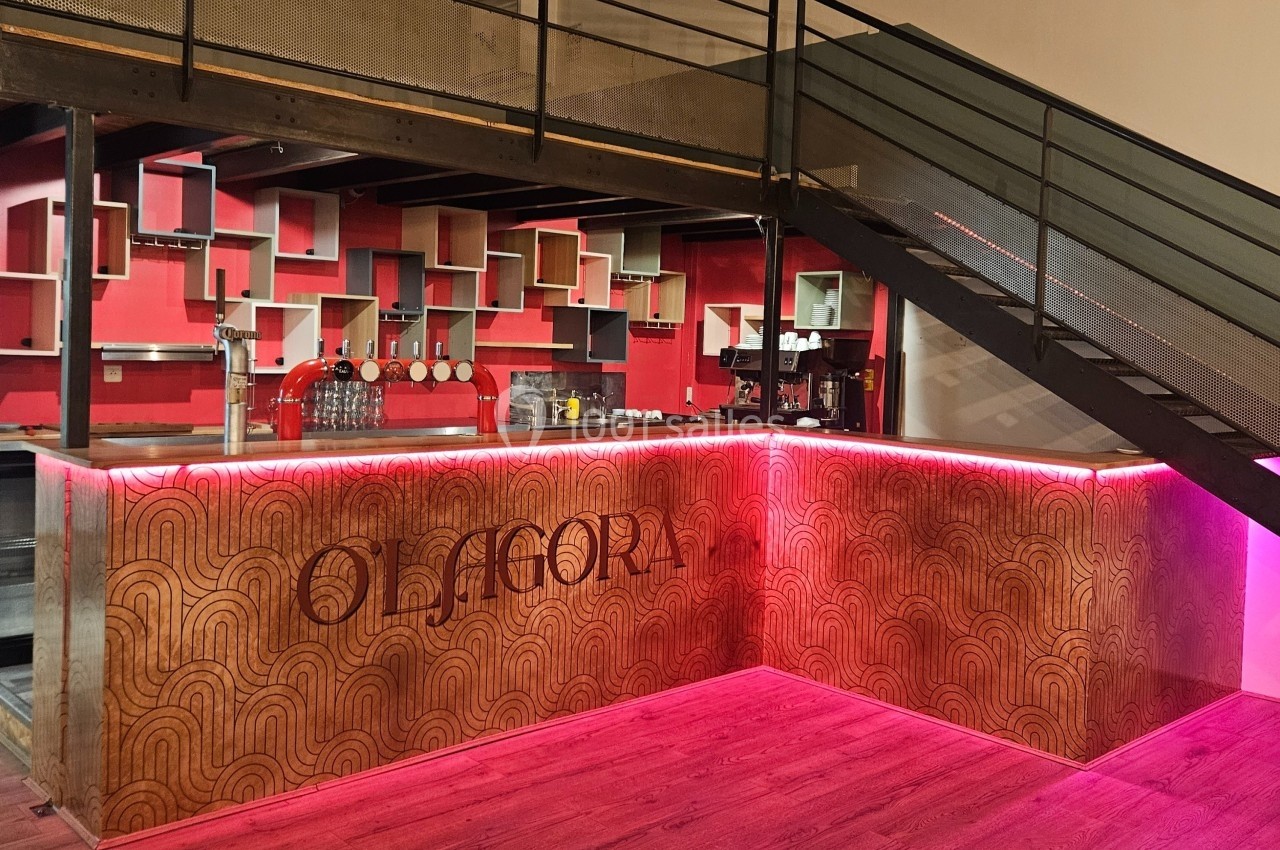 Bar moderne avec comptoir en bois gravé, étagères géométriques rouges et escalier métallique adjacent.