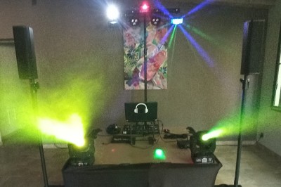 Miniature DJ Ventabren (Bouches-du-Rhône) - Provence Event #4 Un DJ en chemise rouge se tient derrière une table de mixage avec des lumières colorées en arrière-plan.