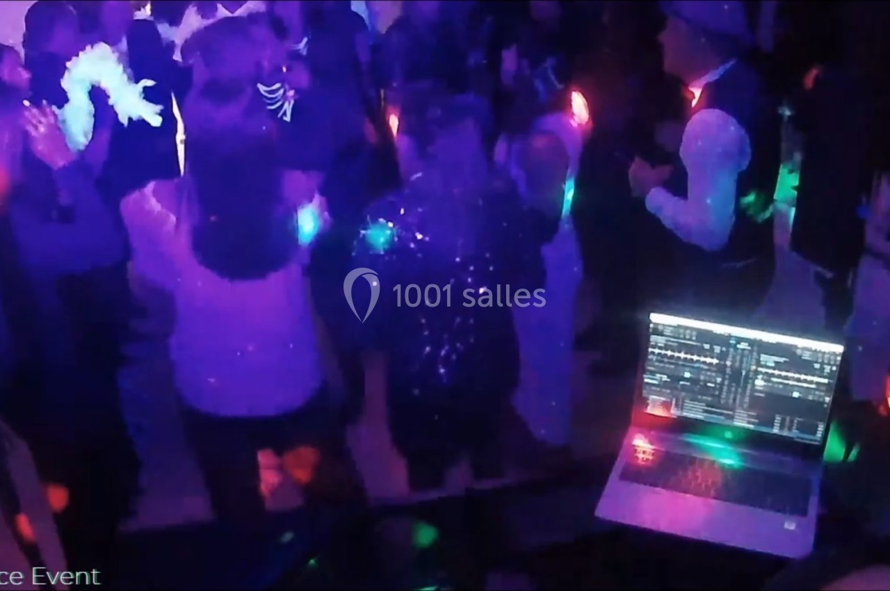 Personnes dansant sous des lumières colorées lors d'une soirée, avec un ordinateur de DJ visible au premier plan.