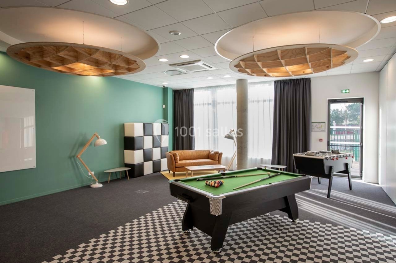 Salle de détente avec table de billard, canapé en cuir, lampes design et grandes fenêtres laissant entrer la lumière…